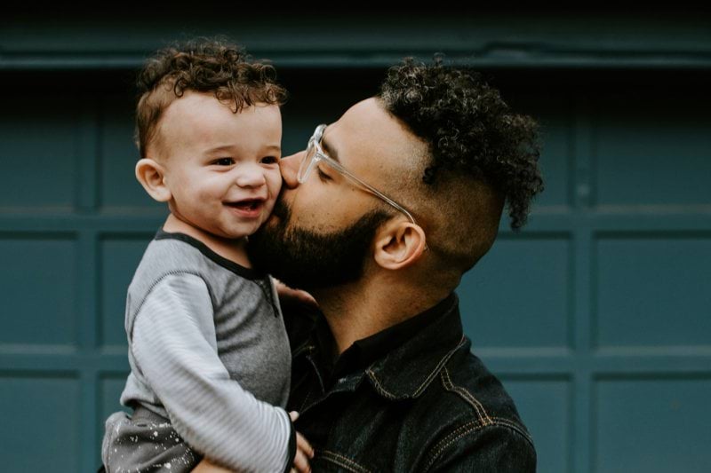 man carrying baby boy and kissing on cheek