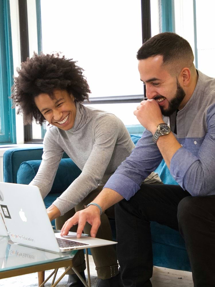 a man and woman sitting on a couch looking at a laptop