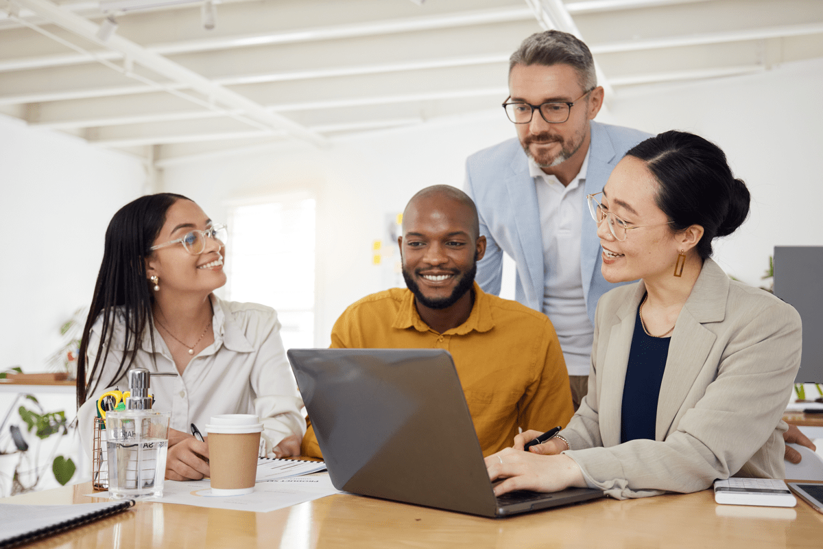 two men and two women grouped around a laptop smiling in a professional workplace