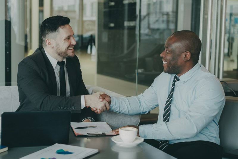 Two businessmen shaking hands across a table.