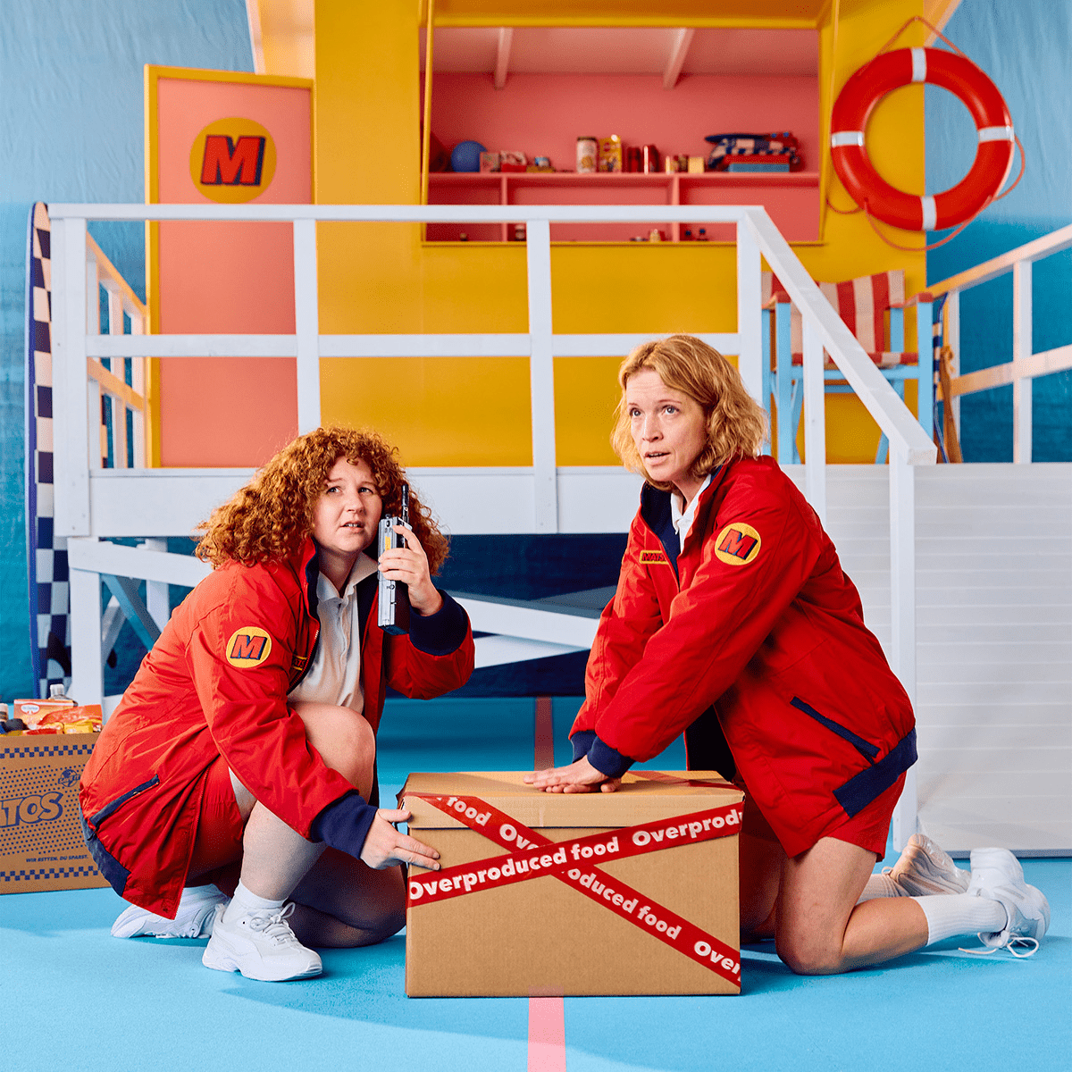 Two food rescuers applying CPR on a box that says 'Overproduced food.'