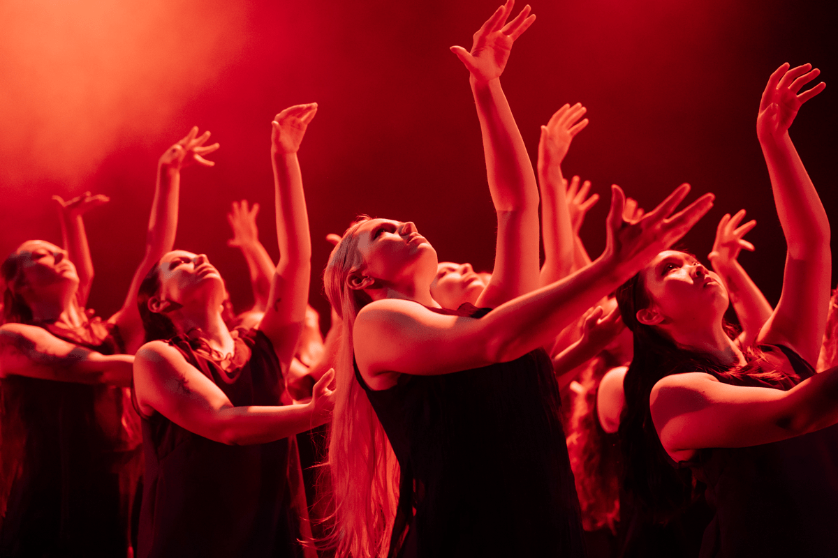 Group of students making gestures with their hands on stage, cast in a red hue
