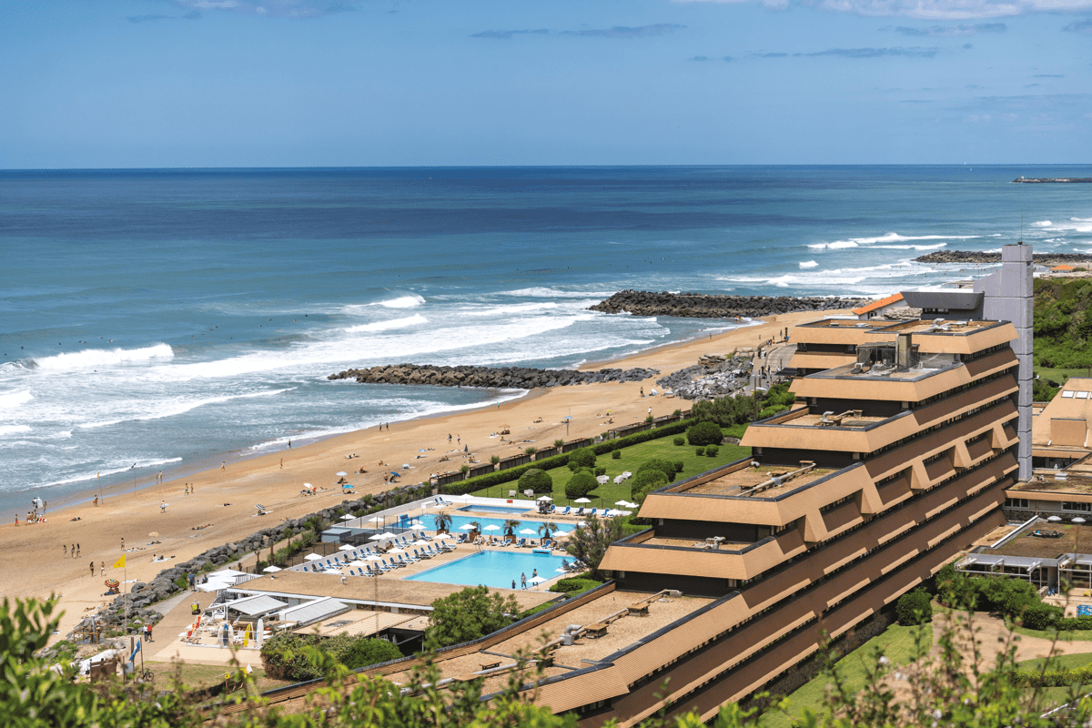 Vue aérienne d'un complexe Belambra au bord de la plage avec l'océan en arrière-plan.