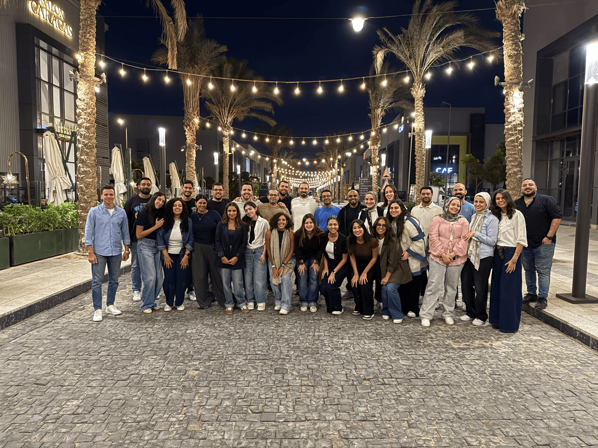 Large group posing outdoors at night on a palm-lined walkway, with string lights overhead and shops in the background.