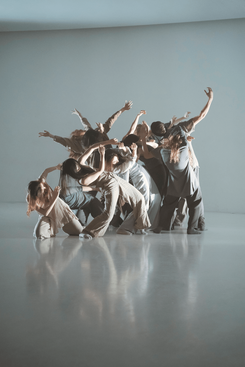A group of students dancing together to form one mass, using their arms to create an overall shape