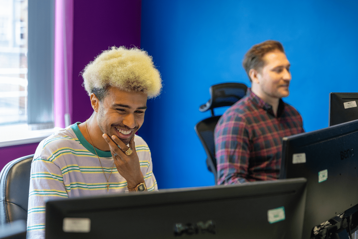 Two colleagues working at desktop computers, one smiling, in a brightly coloured office