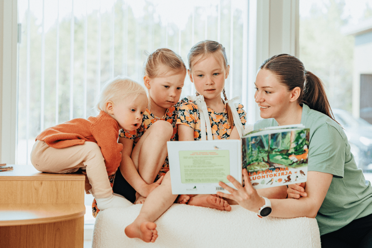 Hoitaja ja lapset lukevat kirjaa