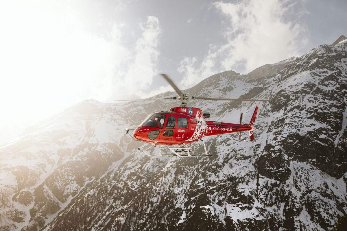 red and white helicopter flying over snow covered mountain during daytime