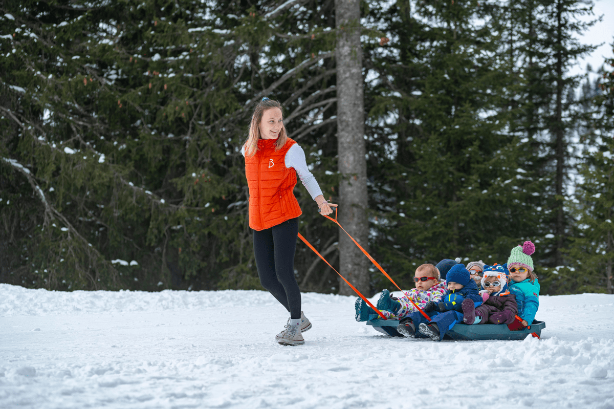 Enfant tiré sur une luge par un adulte à travers une forêt enneigée.