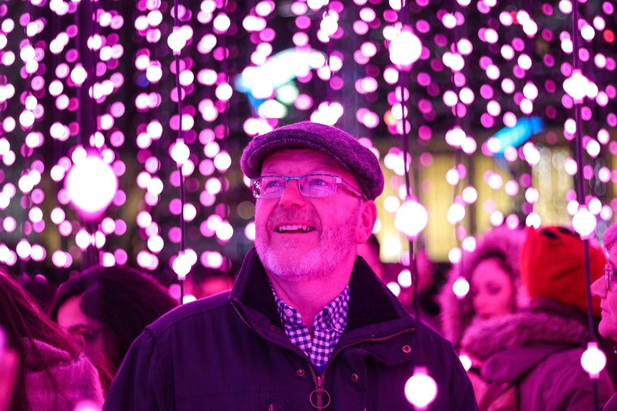 man in black jacket looking at the purple string lights