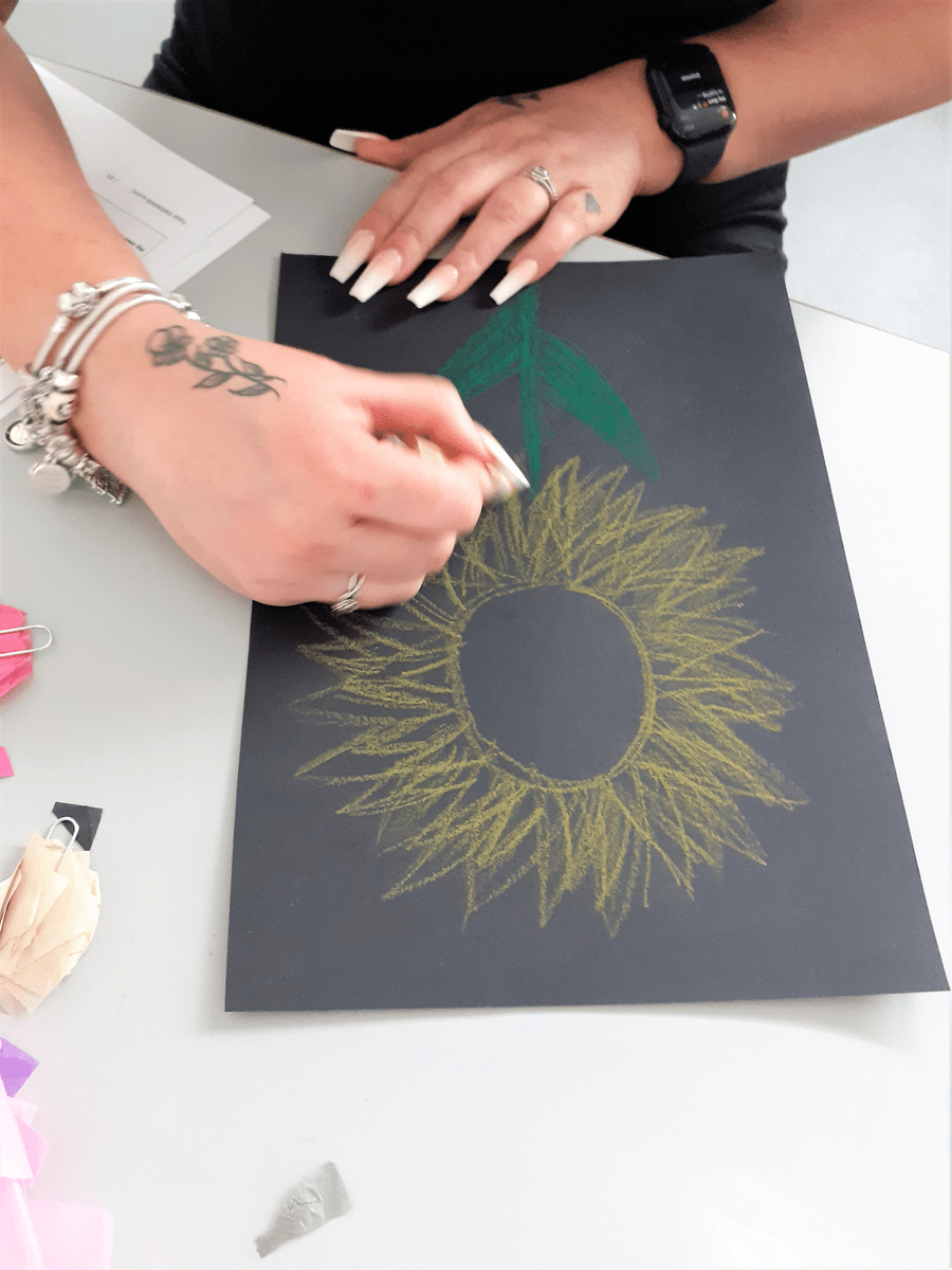 Hands drawing a sunflower on black paper