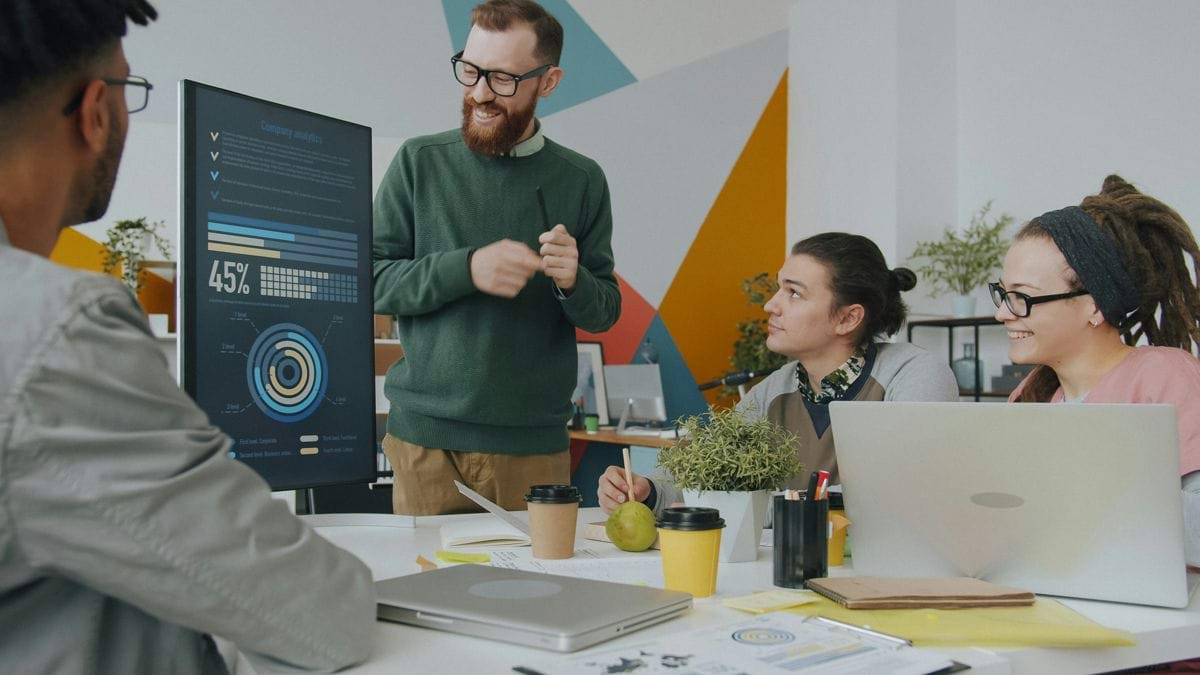 A man presenting data on a vertical monitor to colleagues in a workspace