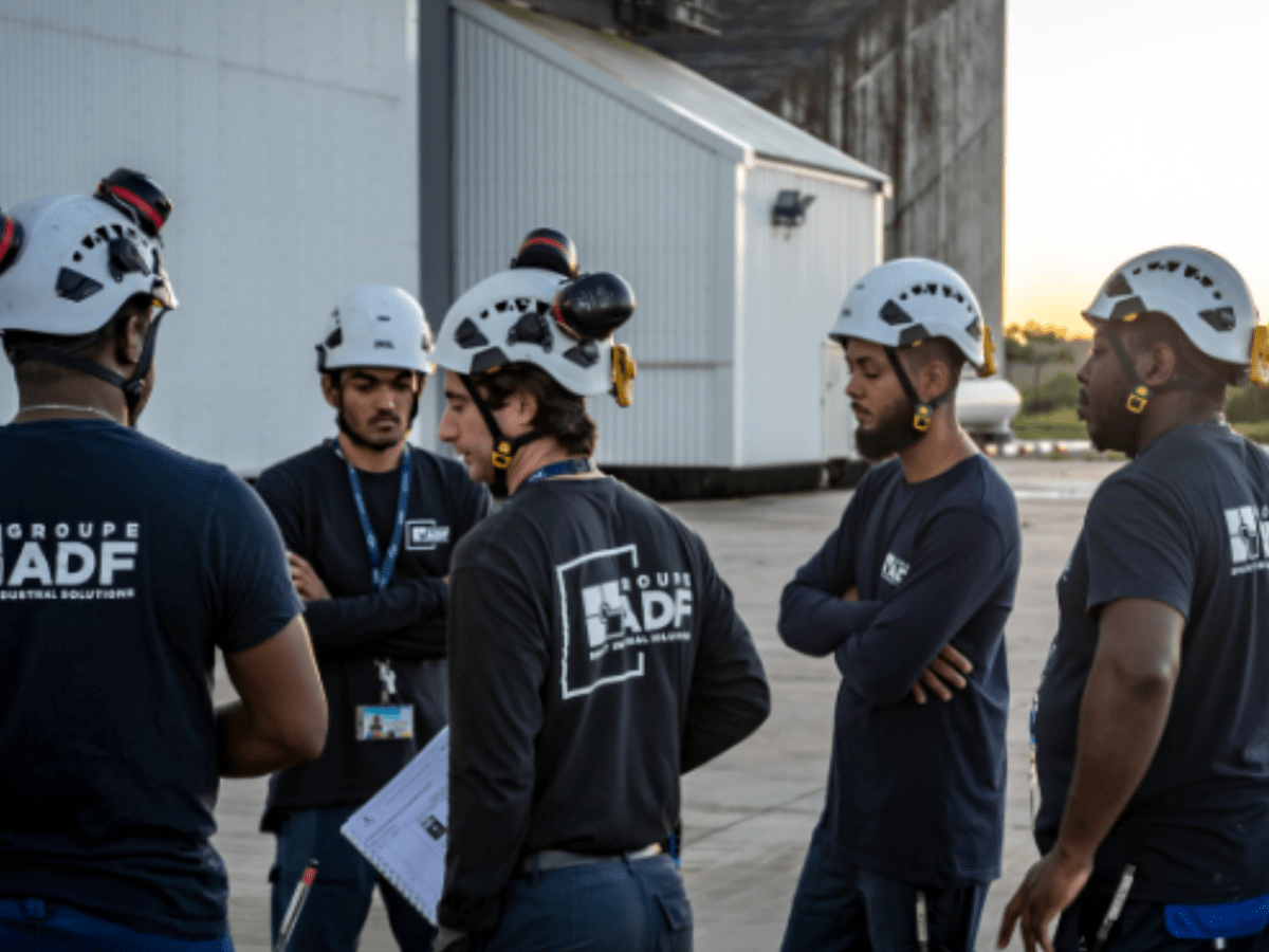 Equipo de colaboradores del Groupe ADF con ropa de trabajo, equipos de seguridad y cascos de protección, reunidos al aire libre en un sitio industrial durante un intercambio.