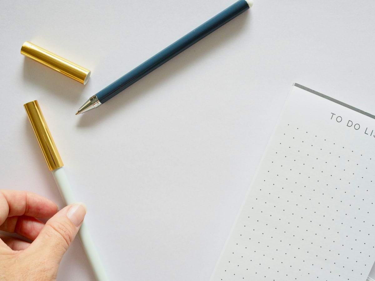 A person holding a pen next to a notebook