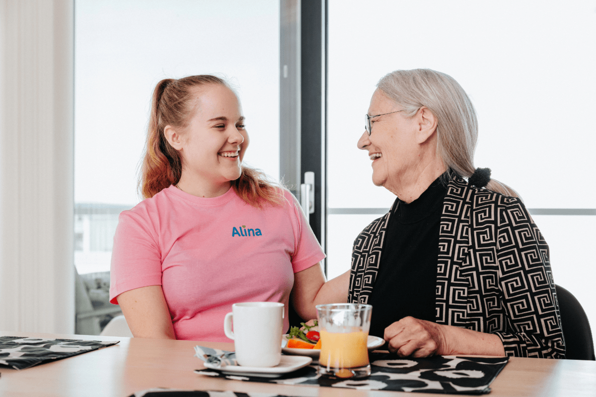 Mummo ja hoitaja istuvat pöydän ääressä välipalalla