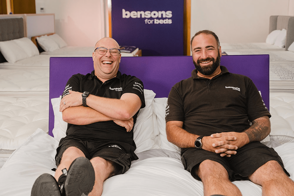Two people smiling and sat on a bed