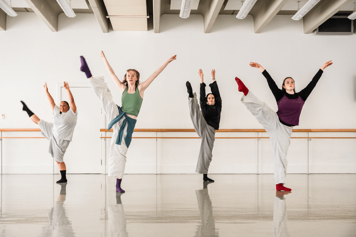Four students in a studio, photographed in the middle a high kick with one leg