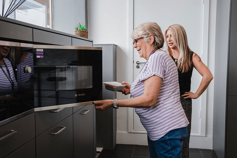 Two women chatting at a microwave in a kitchen
