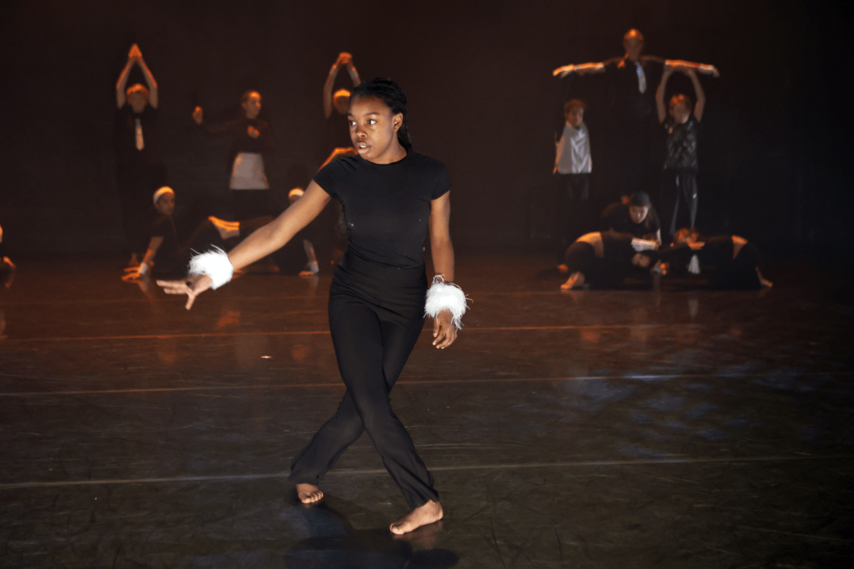 Young dancers all striking poses on stage, with one student in the foreground and others making shapes in the background