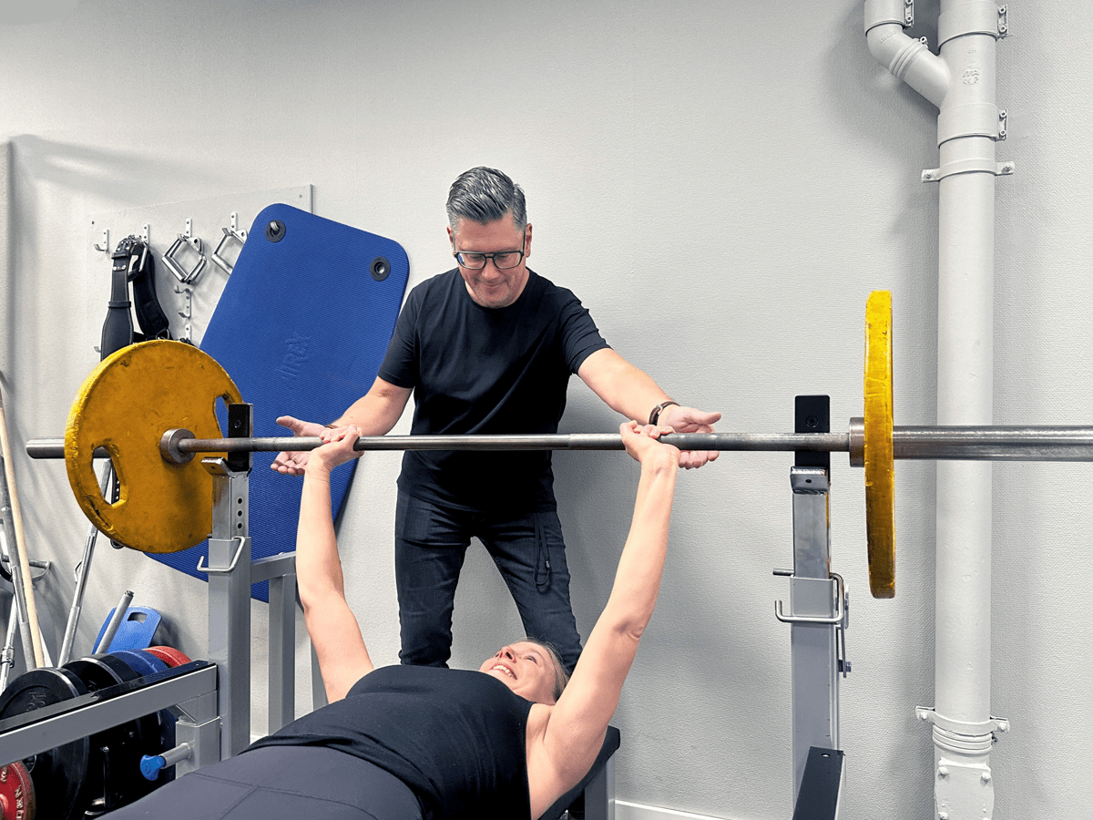 Man hjälper kvinna med skivstång i ett gym