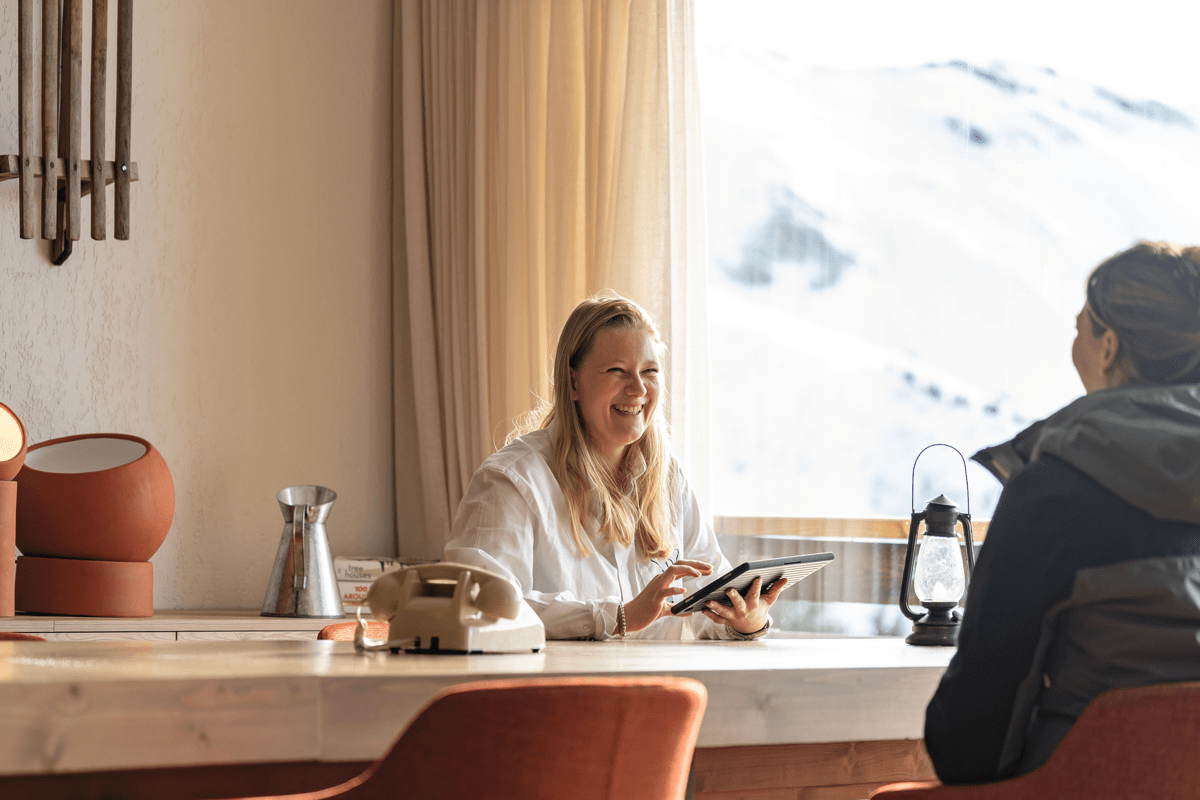 Femme et homme discutant à une table dans une chambre d'hôtel avec vue sur les montagnes enneigées.