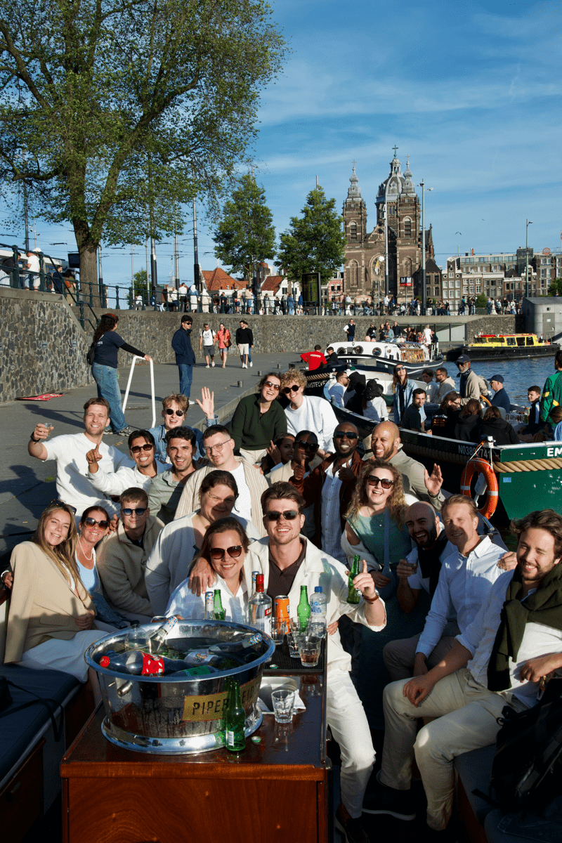 Gezellige teamuitje van Morgan Recruitment Group consultants op een grachtenboot in Amsterdam, met de Sint-Nicolaaskerk op de achtergrond. Employer branding en bedrijfscultuur.