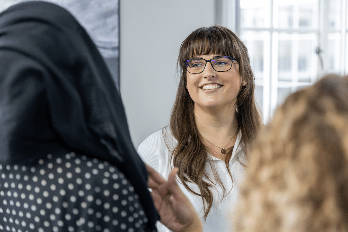 Woman with glasses smiling while talking to colleagues in an office.