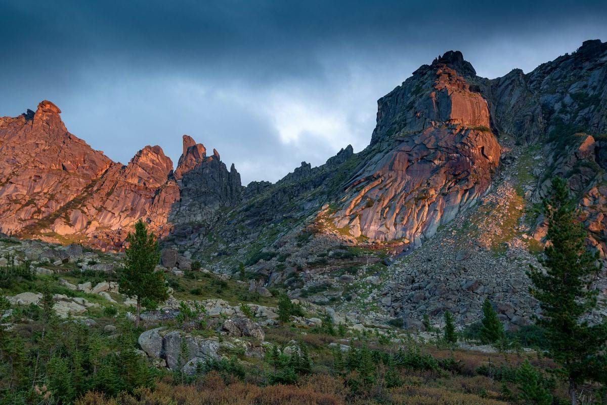 A mountain range with trees and rocks under a cloudy sky