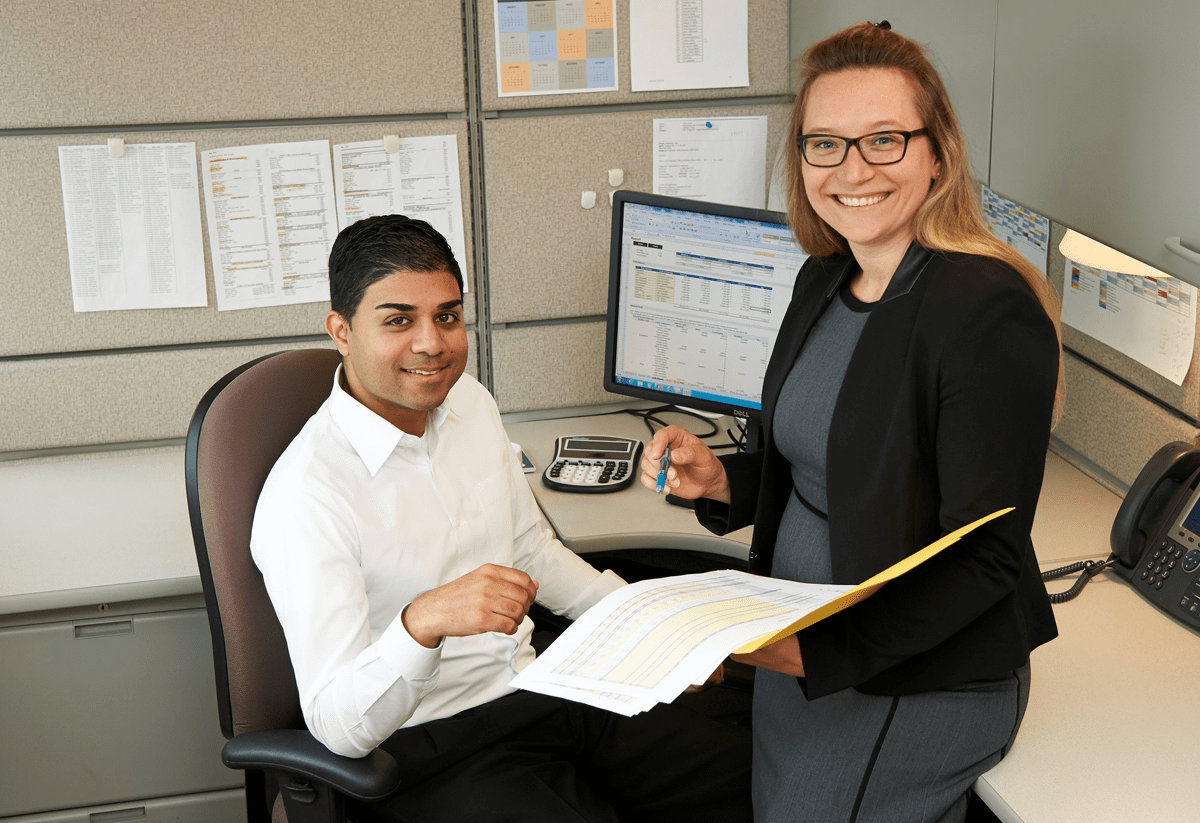 Two smiling employees posing in a brightly-lit, modern office.