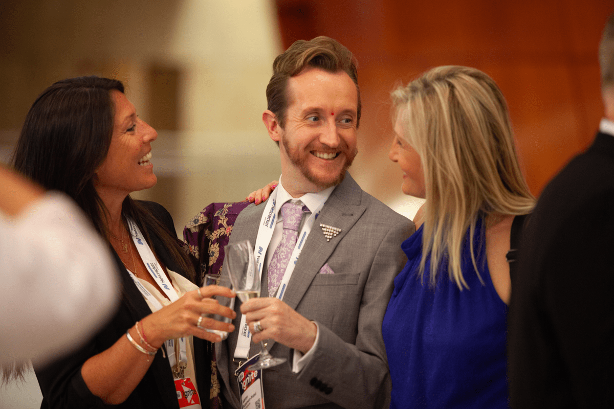 Three TMF colleagues holding champagne glasses, talking and laughing at an event.