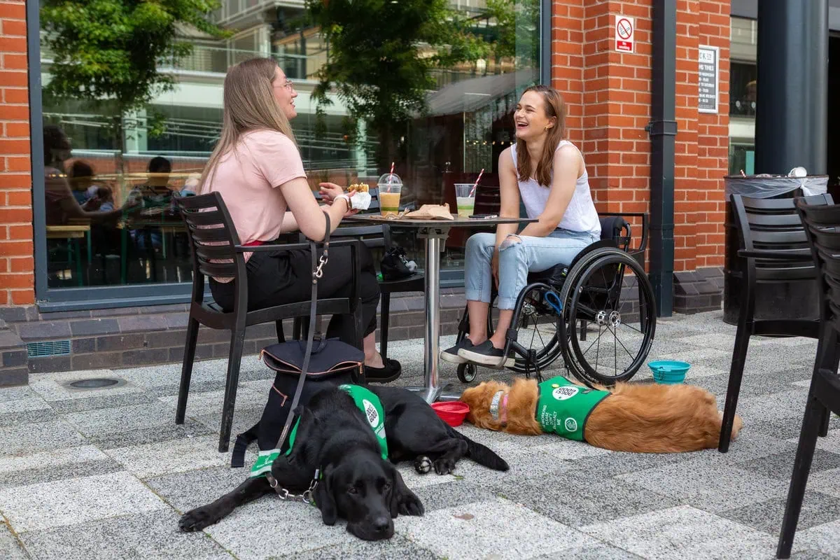 Two women having coffee outside cafe with dogs lying on floor next to table