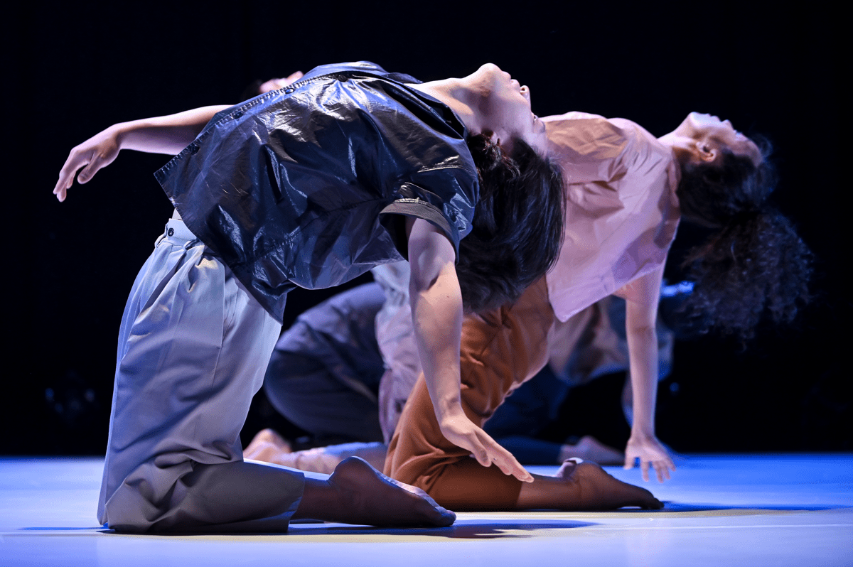 Dancers on stage in purple, pink and blue hues striking a pose with their backs arched.