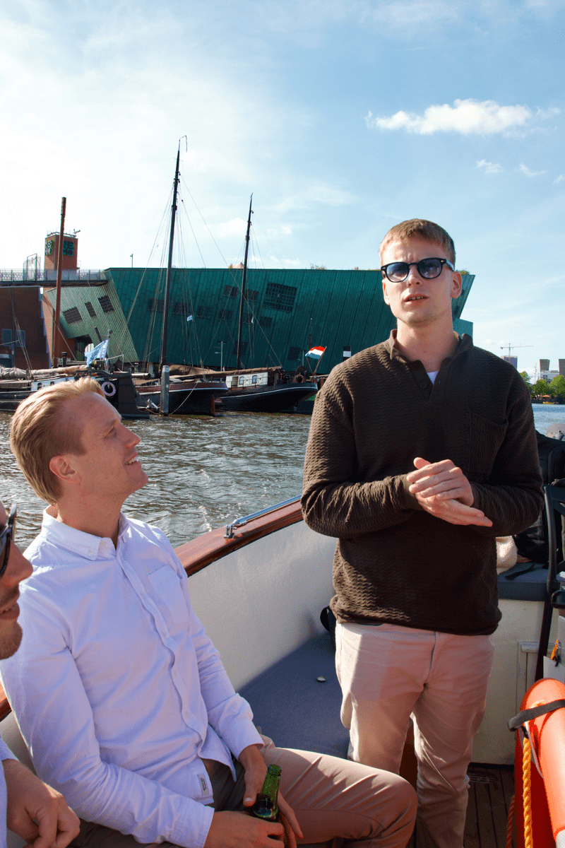 Twee Morgan Recruitment Group consultants op een grachtenboot in Amsterdam, met uitzicht op het NEMO Science Museum en historische zeilschepen