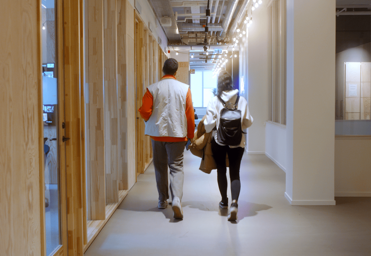 Two employees walking together in the corridors of the office wearing their bags and coats getting ready for a day in the office