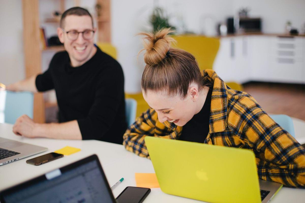 man and woman laughing while sitting in front of laptops