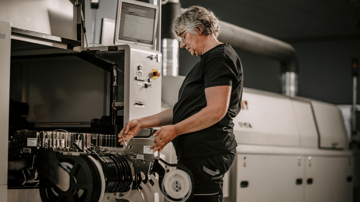 Mitarbeiterin steht an einer Bestückungsmaschine