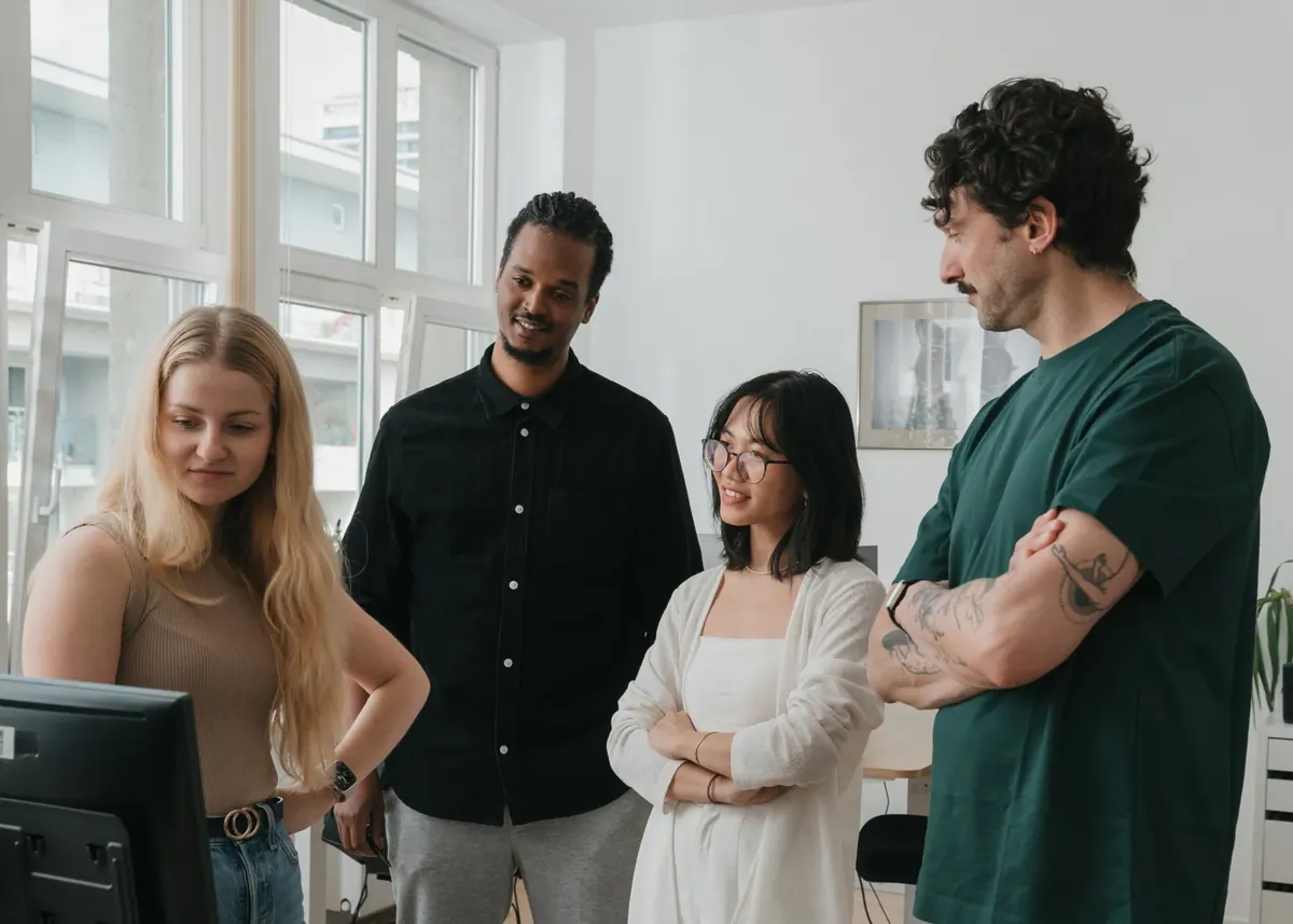 Four colleagues standing together in an office, discussing work while looking at a computer screen.