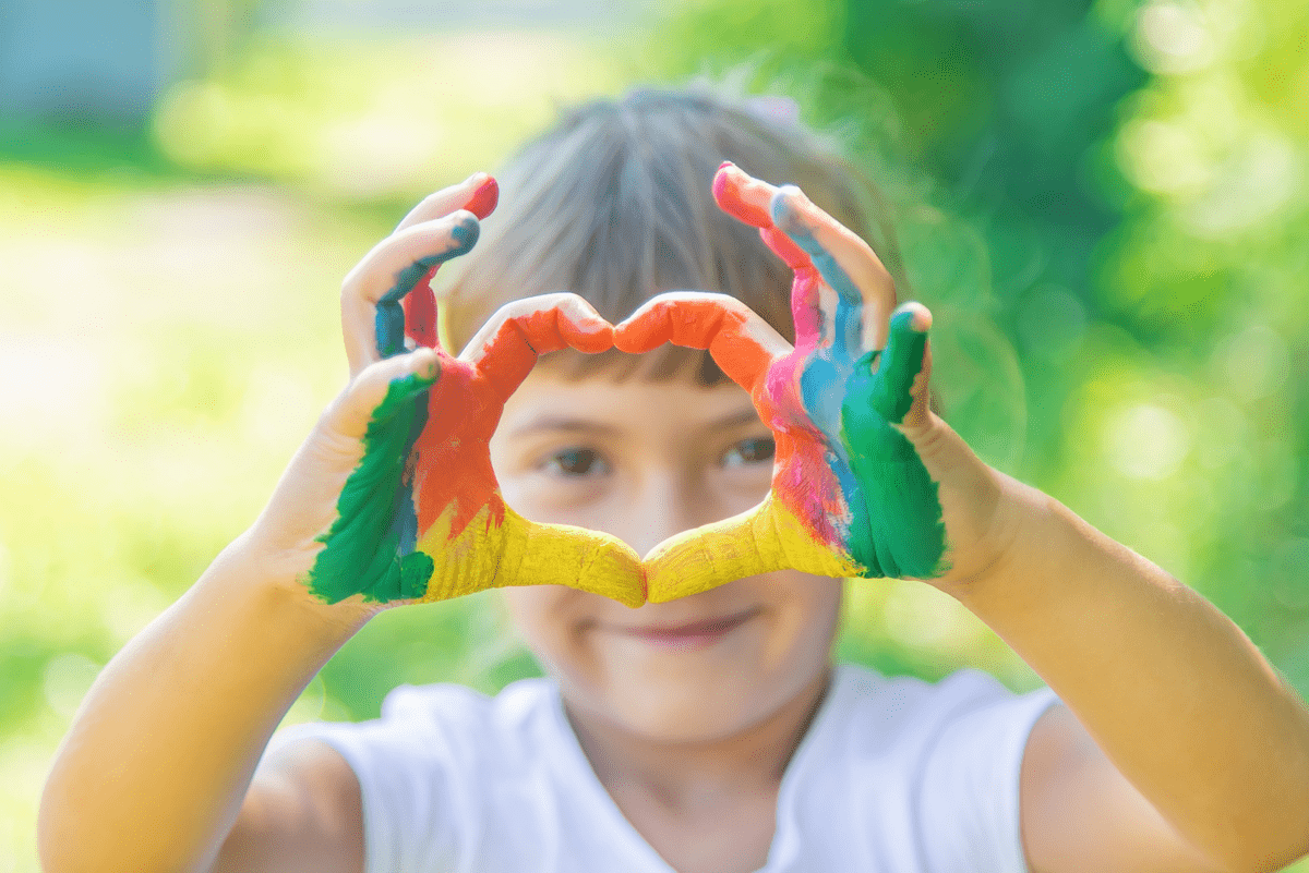 	Ett barn med målade händer gör ett hjärta med fingarna