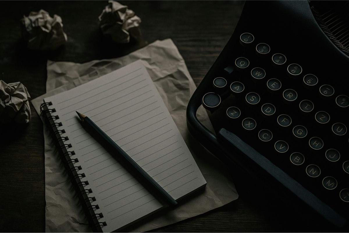 A typewriter, notepad, and crumpled paper are shown.