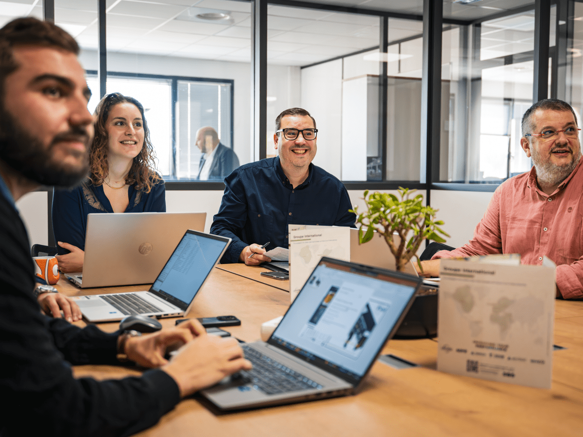 Een team van medewerkers in vergadering in een modern kantoor, in overleg rond laptops in een samenwerkingsgerichte en gezellige sfeer.
