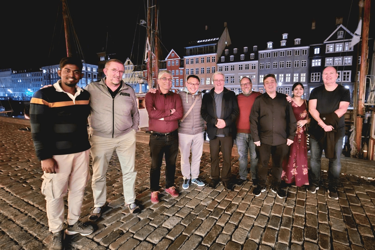 A mixed group of TMF colleagues and members stand outside on a cobbled street at night with houses showing in the background.