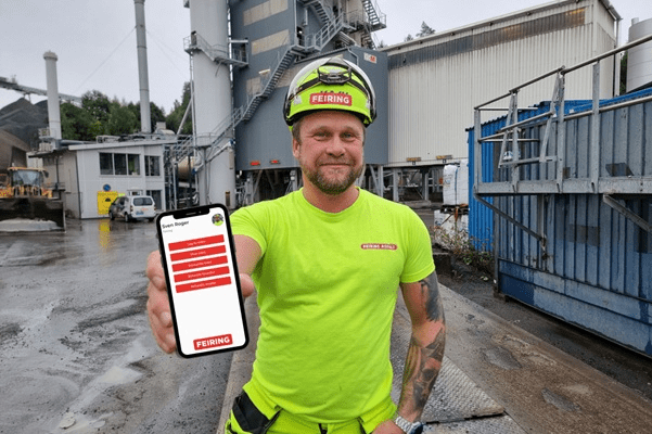 Fornøyd kunde på anleggsplass som viser frem appen bygget av Excito på mobiltelefon. Mann i annlegsklær med Franzefoss logo på gul t-skjorte og hjelm. 