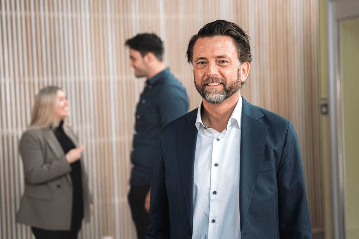 Grunder Håkon Samnøy smilende i forkant. To andre Excitokonsulenter ute av fokus lengre bak i bildet.