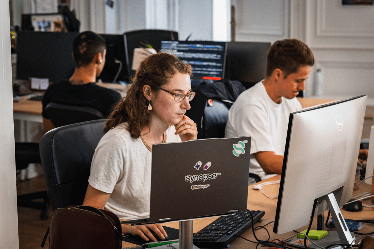Open space, une collègue concentrée derrière un ordinateur portable aux autocollants Synapse