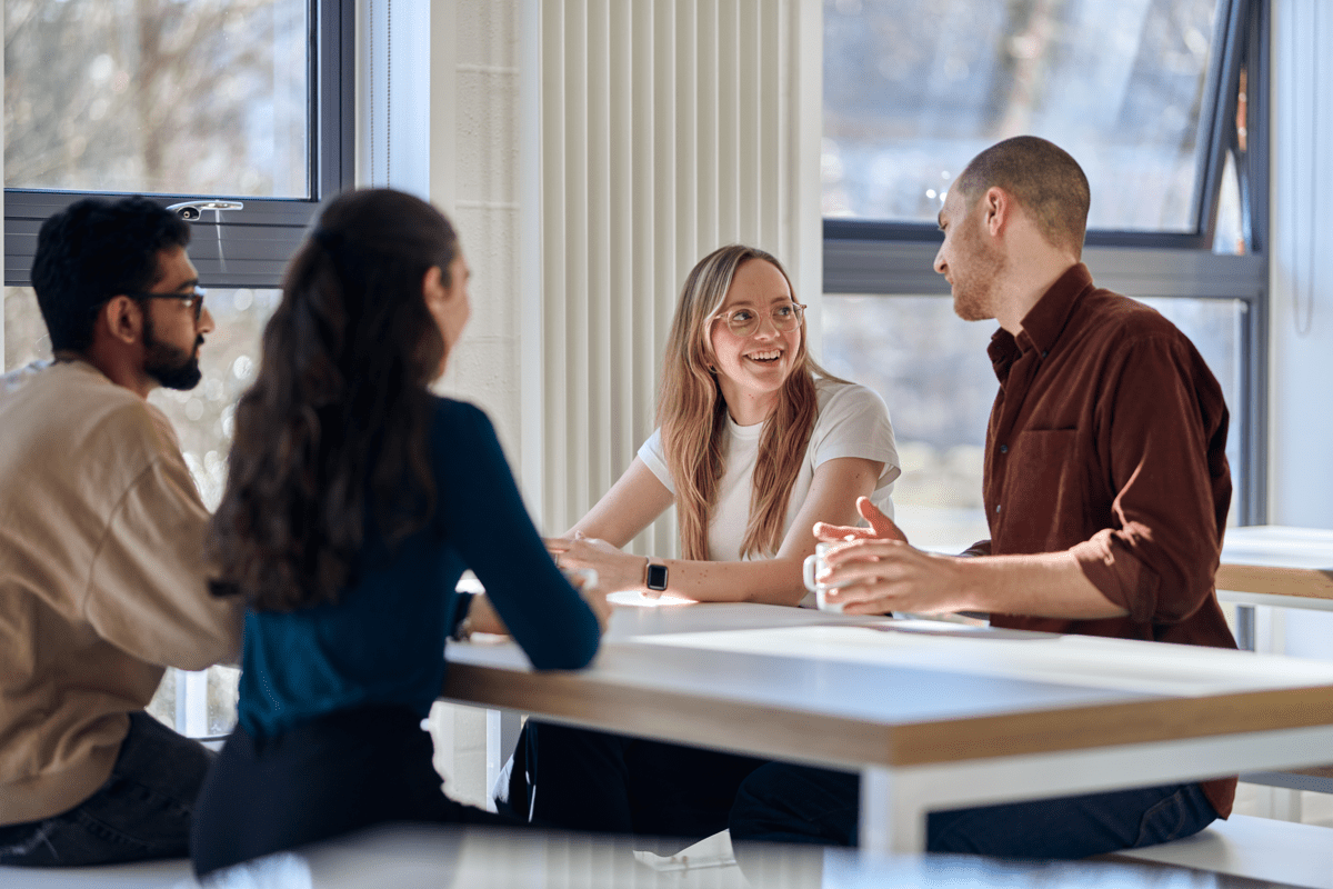 Four Crux employees sit around a table, interacting and talking together during a collaborative meeting.