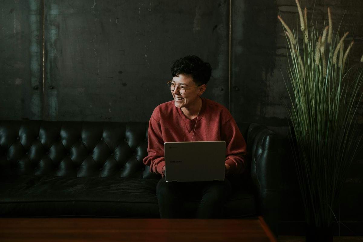 smiling man using laptop computer while sitting on black leather sofa