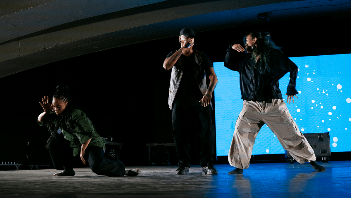 Three members of SAY performing together. Two are holding a mic and one is crouching.