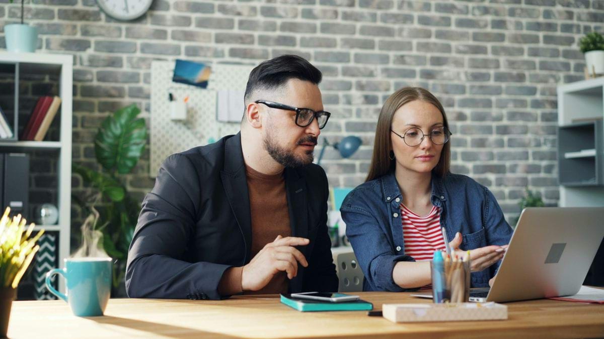 a man and a woman sitting at a table looking at a laptop