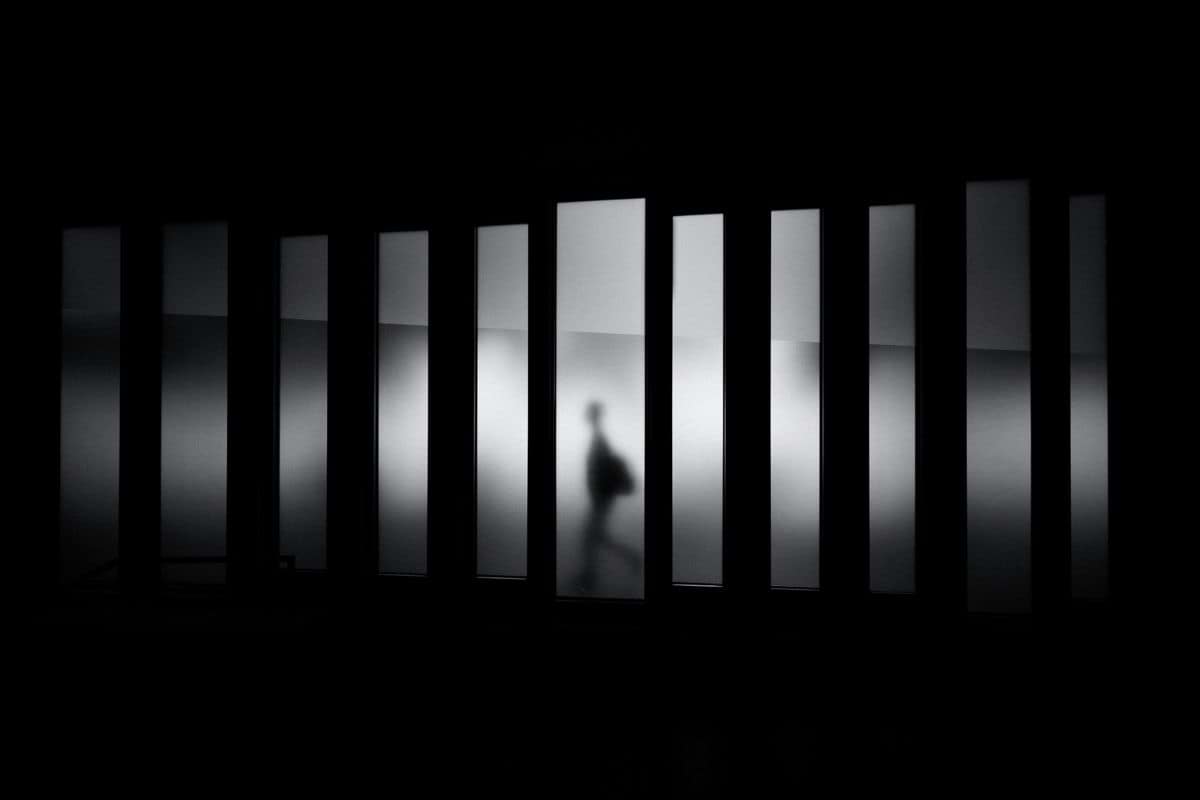 A person in silhouette walking behind a row of vertical frosted glass panels