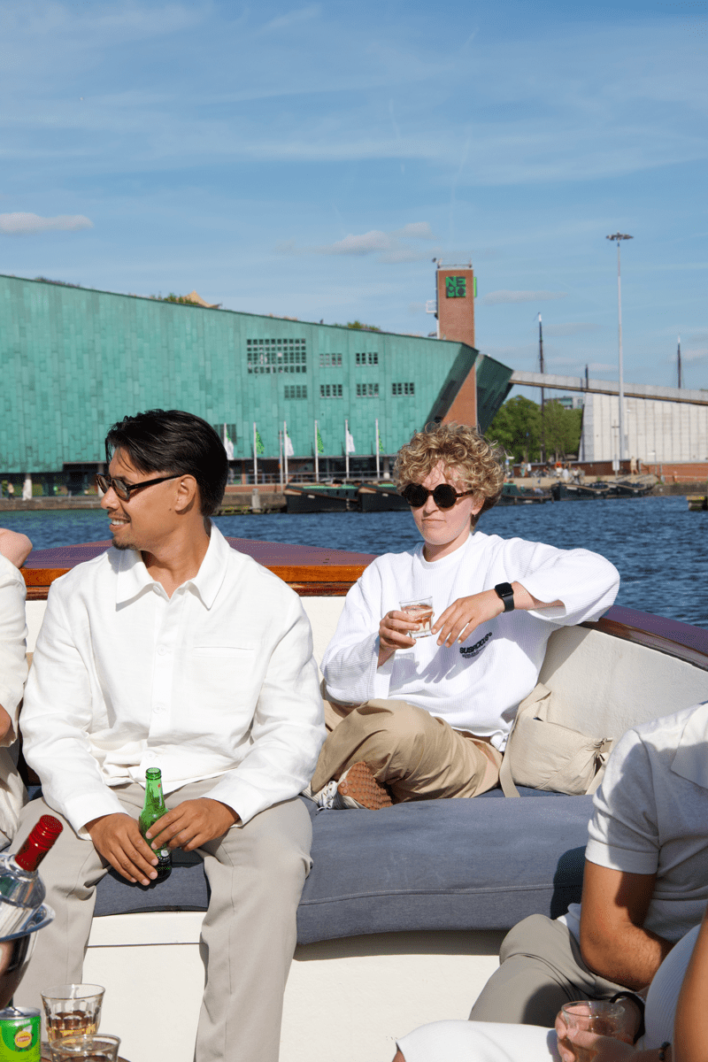 Collega's van Morgan Recruitment Group genieten van drankjes op een boot tijdens een sociaal evenement op de grachten van Amsterdam, bij het NEMO Science Museum.
